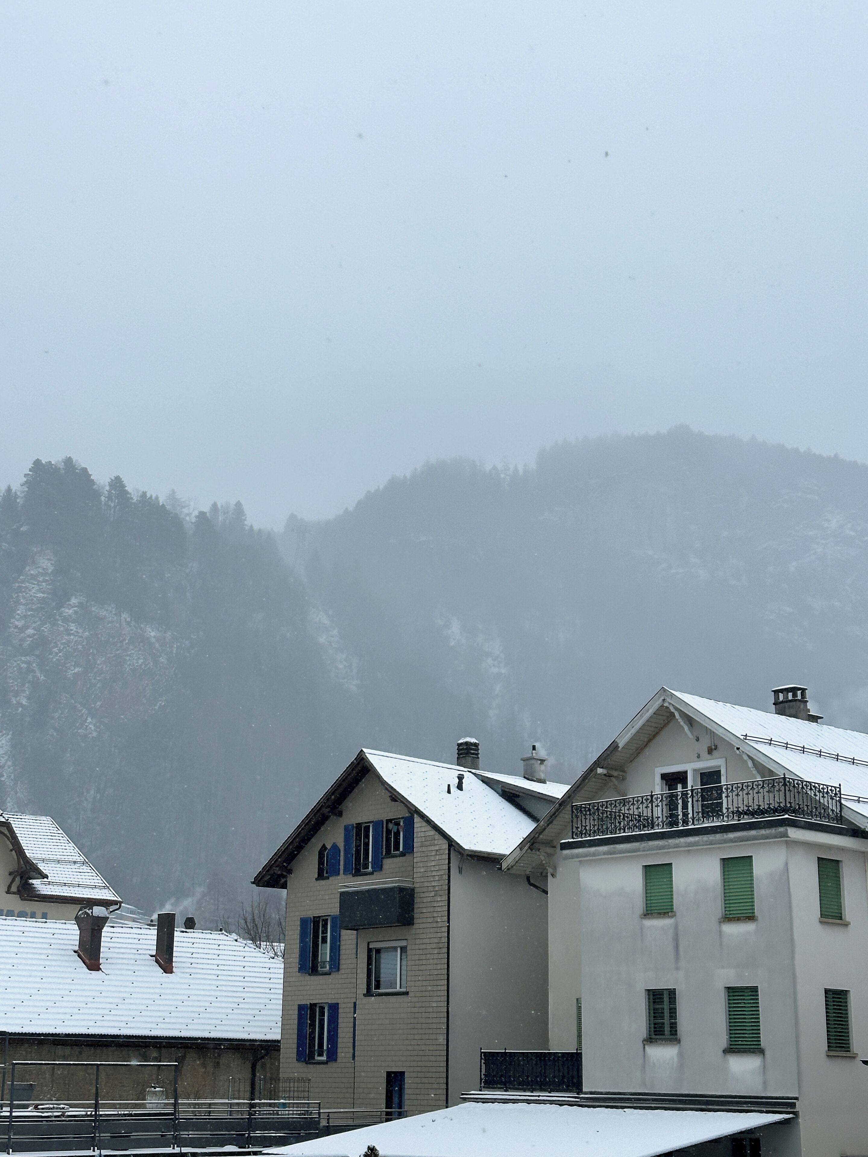 Un edificio con techo nevado, un balcón y montañas al fondo.