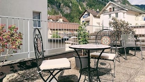 Ein Balkon mit Tisch und Stühlen, mit Blick auf eine gebirgige Landschaft.