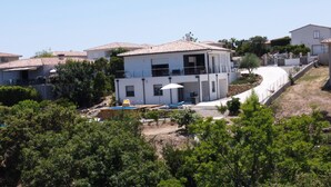 Ein modernes, zweistöckiges Haus mit Swimmingpool, umgeben von Grünflächen und weiteren Häusern.