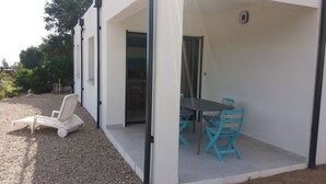 Eine moderne Terrasse im Freien mit Tisch und Stühlen, einem weißen Stuhl und einem Kiesgrund.