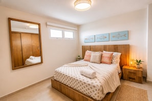 Une chambre à coucher avec un grand lit, une tête de lit en bois, une table de chevet avec une lampe, un miroir et des œuvres d’art accrochées au mur.