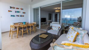A modern living room with a dining area, large glass sliding doors leading to a balcony, and decorative fish wall art. - LuxuryCondo| Beachfront| AmazingView | FastWifi (Juan Dolio)