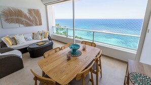 A spacious balcony with a view of the ocean, a wooden dining table with chairs, a sofa with patterned cushions, and a decorative wall piece. - LuxuryCondo| Beachfront| AmazingView | FastWifi (Juan Dolio)
