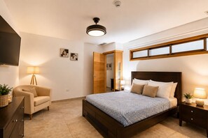 Un dormitorio con cama, una silla, una mesita de noche, una lámpara, un ventilador de techo y una ventana.