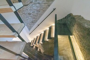 Een modern interieur met een stenen muur, een trap met witte leuningen en een plafond met een bijzondere textuur.