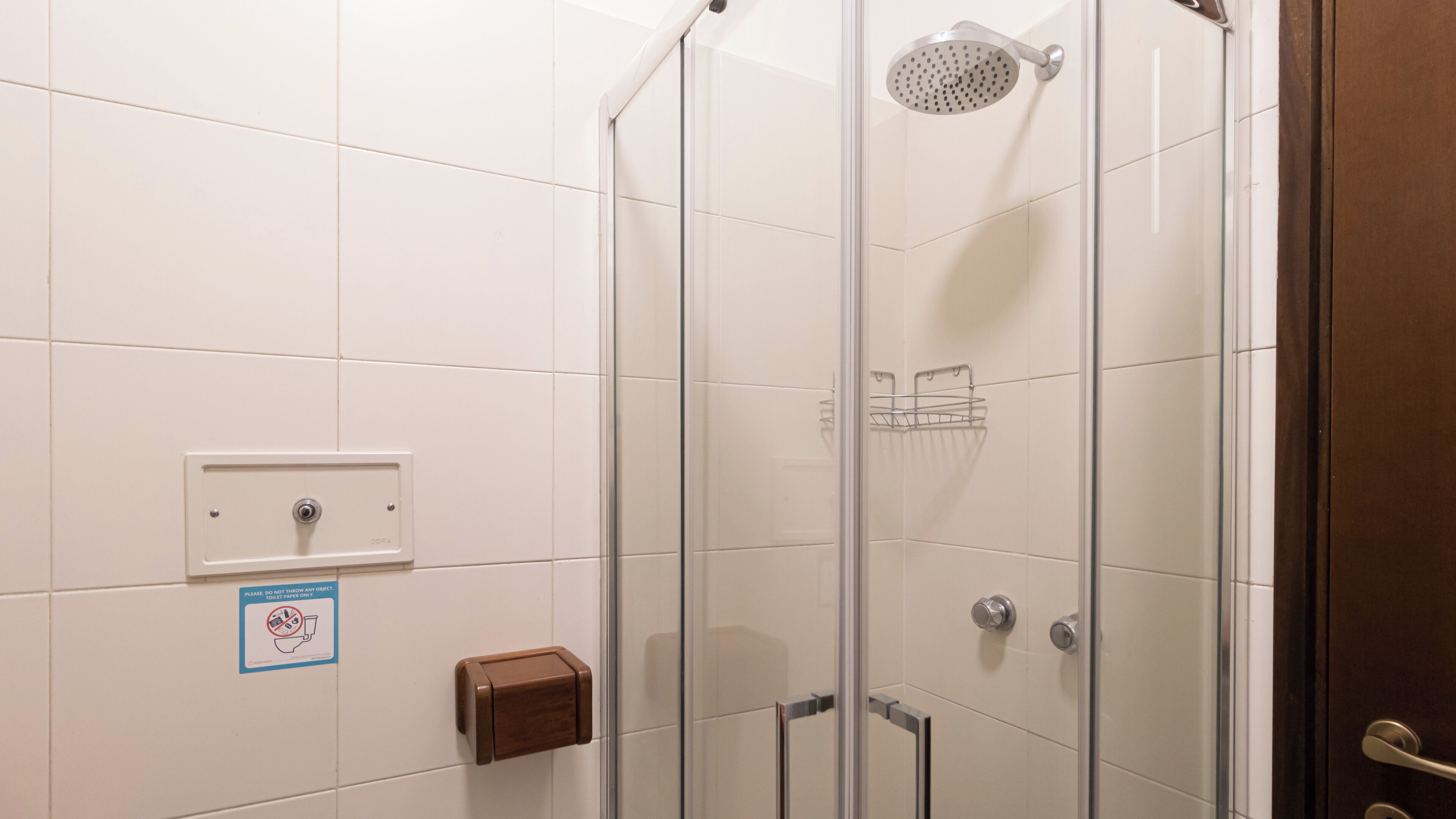 Une douche fermée par des parois en verre, dotée d’un pommeau de douche à main, d’un distributeur de serviettes et d’un porte-savon fixé au mur.