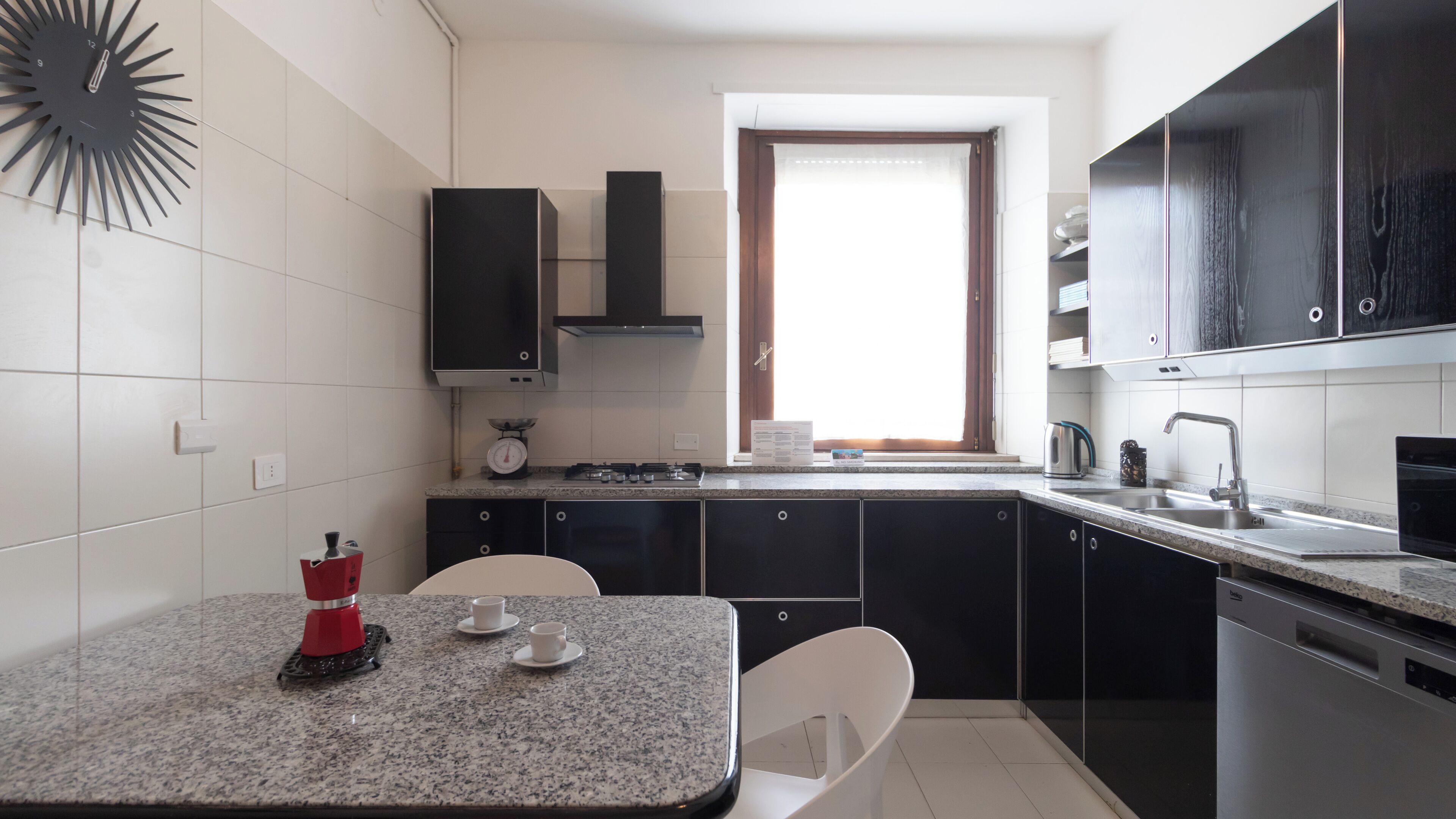 A modern kitchen with a granite countertop, black cabinets, a built-in oven, and a window with a view.