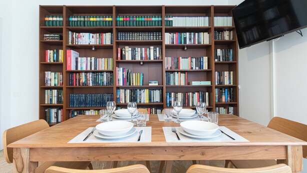 A dining area with a wooden table set for two, surrounded by bookshelves filled with books. - Italianway - Palazzi 6 C (Milan)