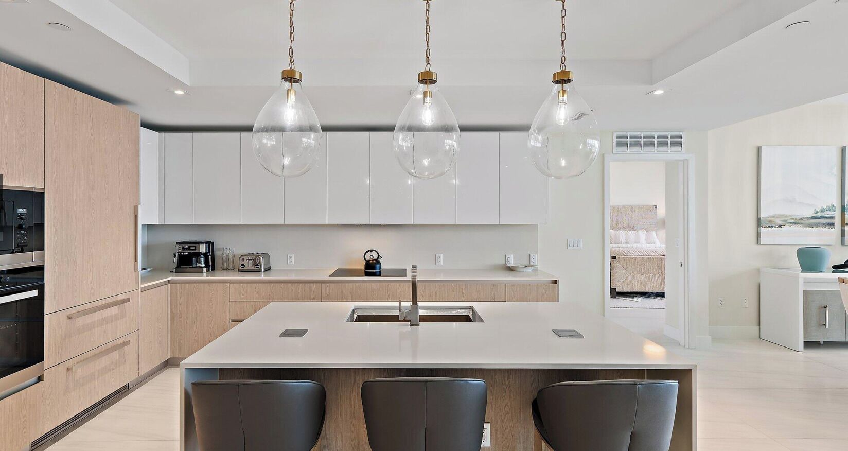 Una cocina moderna con una isla central, luces colgantes y vistas al área de estar.