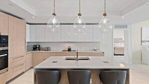 A modern kitchen with a central island, pendant lights, and a view to the living area. - Luxury Amrit Ocean Resort - 2BDR Condo (Riviera Beach)