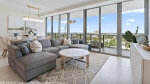 A modern living room with a sectional sofa, a round coffee table, and large windows offering a city view. - Luxury Amrit Ocean Resort - 2BDR Condo (Riviera Beach)