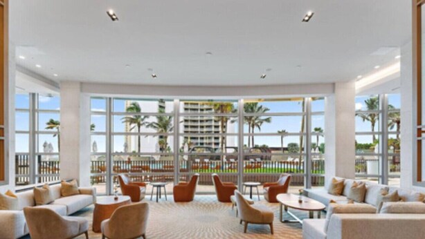 A spacious lobby with a checkered carpet, sofas, armchairs, and tables. Large windows offer views of palm trees and a building across the street. - Luxury Amrit Ocean Resort - 2BDR Condo (Riviera Beach)