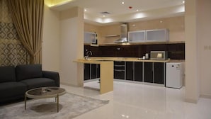 A modern kitchen with a central island, black cabinets, and a small refrigerator. - شقق الشرفة للشقق المفروشة -AlSHORFA FURNISHED APARTMENT (Riyadh)