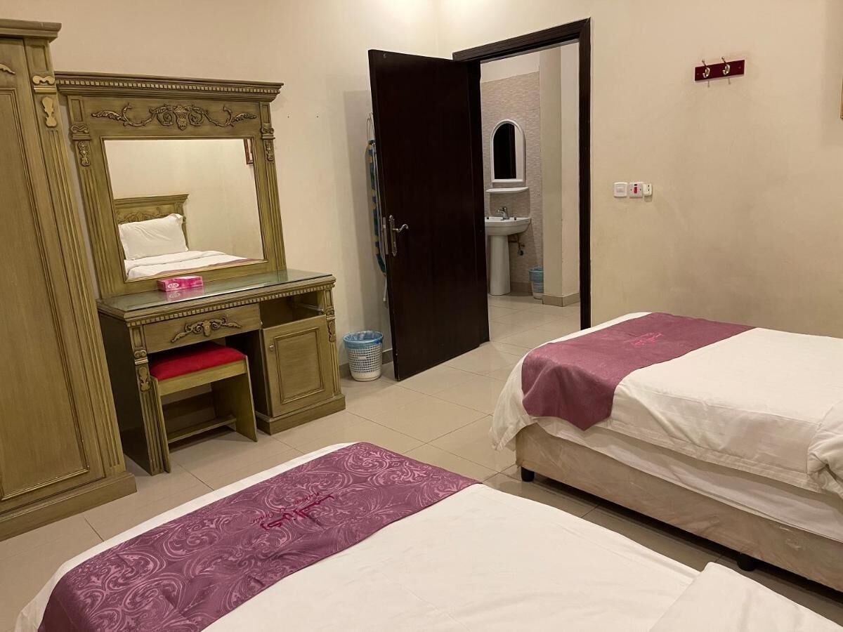 A hotel room with two beds, a wooden desk with a chair, a mirror, and a bathroom visible through an open door.