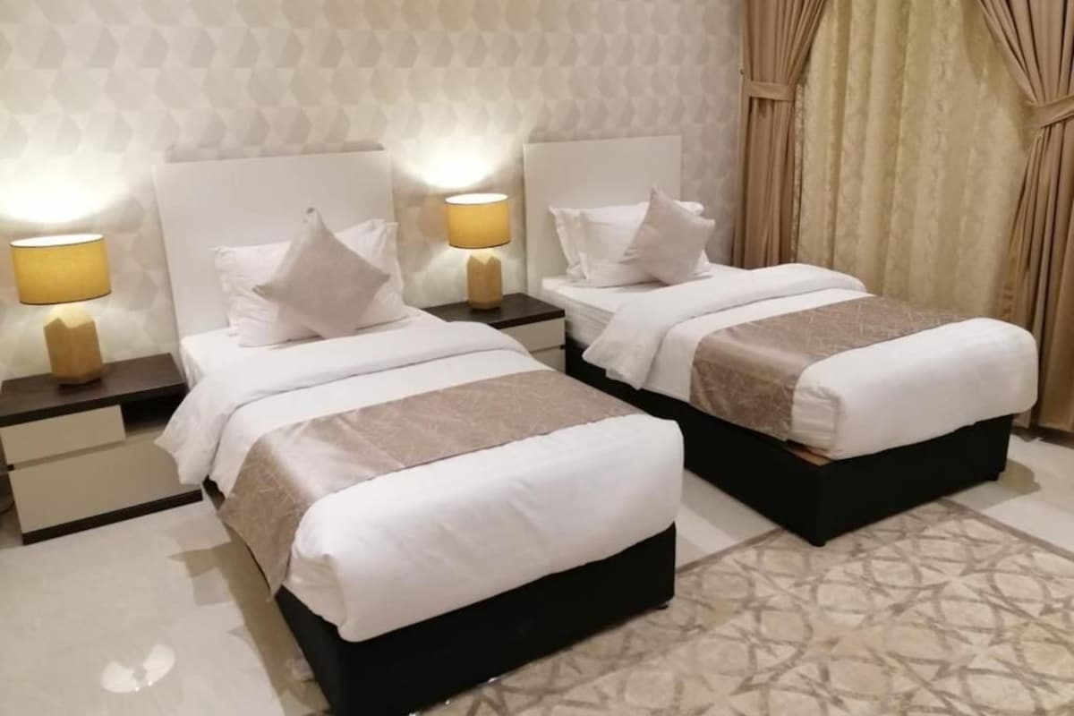 A hotel room with two beds, each with a white headboard, a bedside table with a lamp, and a patterned rug.