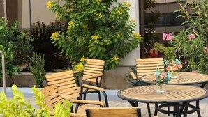 An outdoor seating area with round wooden tables and chairs, surrounded by various plants and flowers. - شقق الشرفة للشقق المفروشة -AlSHORFA FURNISHED APARTMENT (Riyadh)