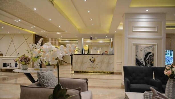 A modern hotel lobby with a reception desk, seating area, and decorative elements like flowers and artwork. - شقق الشرفة للشقق المفروشة -AlSHORFA FURNISHED APARTMENT (Riyadh)