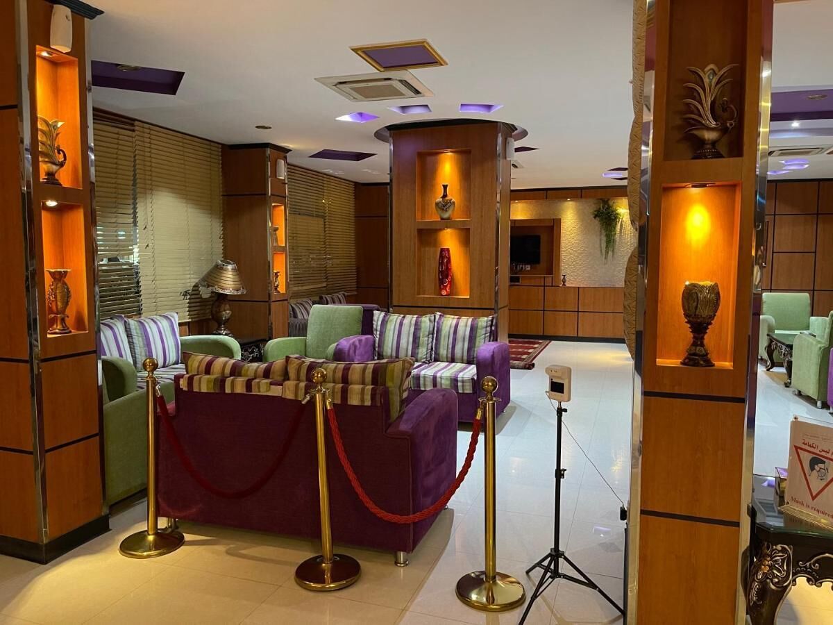Un hall d’entrée avec un ensemble de canapés violets, des panneaux de bois et une barrière faite d’une corde rouge.