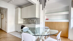 A modern kitchen with white cabinets, a glass dining table, and white chairs. - Whitewood Residence (Athens)