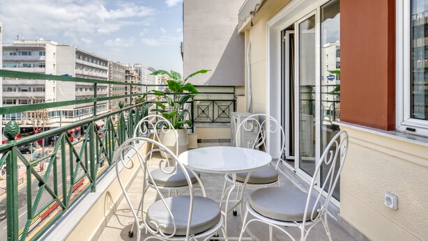 A balcony with a table and chairs, a potted plant, and a view of the cityscape. - Whitewood Residence (Athens)