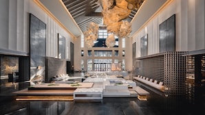 En rummelig lobby med et moderne design, der inkluderer et centralt siddeområde, store vinduer og en unik lofts skulptur.