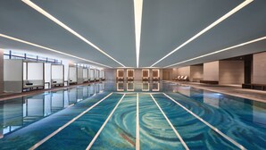 En moderne indendørs swimmingpool med krystalklart vand, liggestole og et loft med lineær belysning.