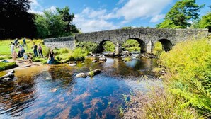 A stone bridge over a clear stream with people walking and cycling nearby.