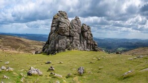 A rocky outcrop with a grassy foreground and distant hills under a cloudy sky.