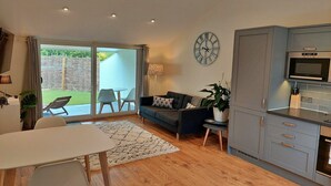 A modern living room with a sofa, a dining table, and a kitchen area with cabinets and a microwave.