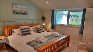 A bedroom with a large bed, a bedside table, a nightstand, a window with curtains, and a painting on the wall. - Cottage in Dartmoor with Private Hot Tub (Bovey Tracey)