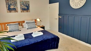 Un lit bien fait, recouvert d’une couvre-lit bleue, agrémenté de deux éléments décoratifs fixés au mur, une porte blanche et un objet décoratif fixé au mur.
