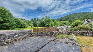 Ein Steinweg führt zu einer Steinsäule mit Holzzaun und einem kleinen Steinhaus.