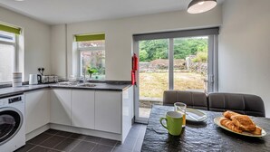 Eine moderne Küche mit integriertem Waschmaschine, ein Essbereich mit Tisch für zwei Personen und eine große Glastür, die zu einem Garten führt.
