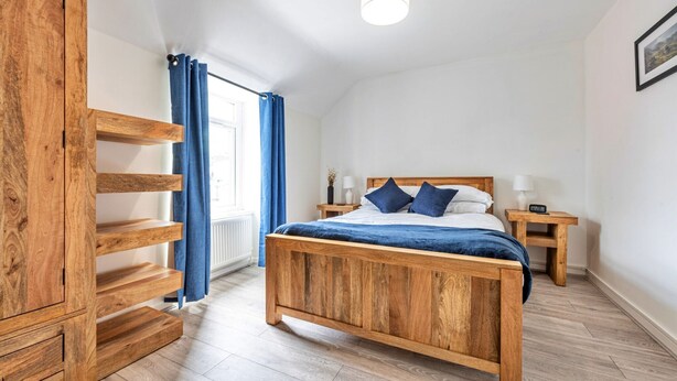 Ein Schlafzimmer mit einem hölzernen Bett, einem Kleiderschrank, einem Nachttisch und einem Fenster mit blauen Vorhängen.
