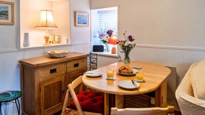 A cozy dining area with a wooden table, chairs, a vase of flowers, and a window with blinds. - Cottage in St Dennis near Eden Project (St Dennis)