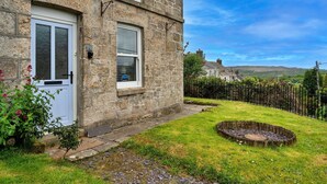 A stone house with a white door and window shutters, a small garden with a circular stone feature, and a metal fence. - Cottage in St Dennis near Eden Project (St Dennis)
