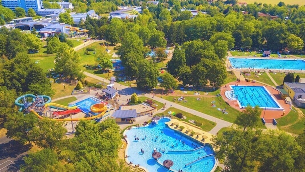 Vue aérienne d’un complexe hôtelier doté de plusieurs piscines, de toboggans aquatiques et d’une grande piscine centrale entourée d’arbres.