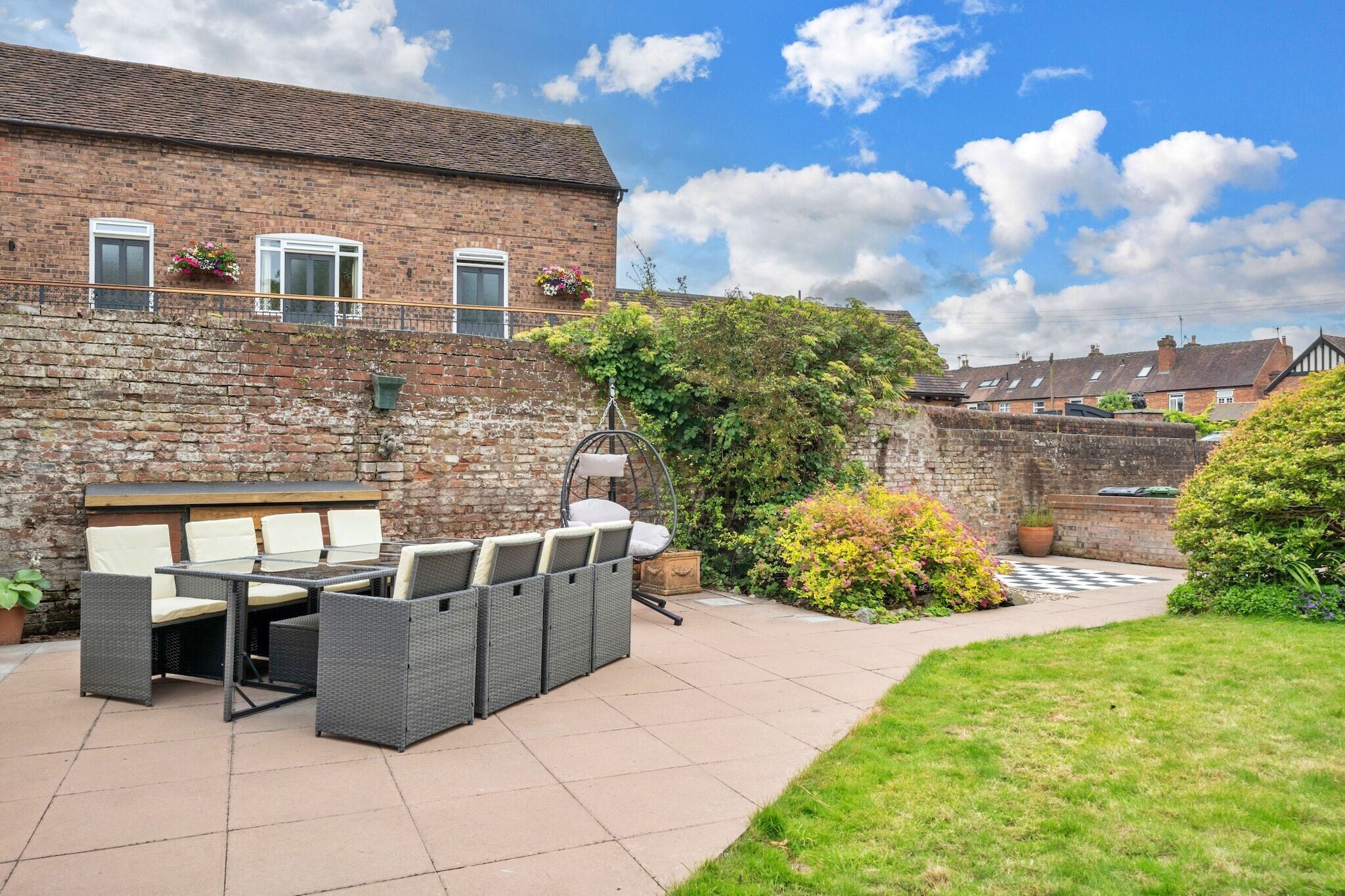 Une terrasse avec des meubles d’extérieur, un bâtiment en briques et un espace jardin.
