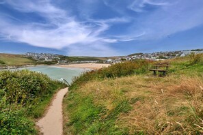 A coastal path leading to a beach with a bench and houses in the background.