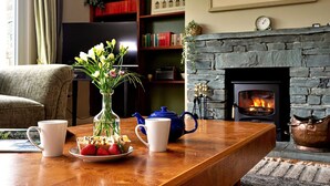 A cozy living room with a fireplace, a coffee table with a teapot, cups, and a plate of strawberries. - Cottage in Grasmere with Lake Access (Grasmere)