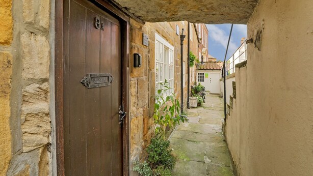 A narrow alleyway with a wooden door, stone walls, and a small garden area. - Cottage in Whitby near Stunning Beaches (Whitby)