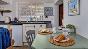 A compact kitchen with a sink, kettle, and coffee maker. There is a dining table with plates and a cup. - Cottage in Whitby near Stunning Beaches (Whitby)