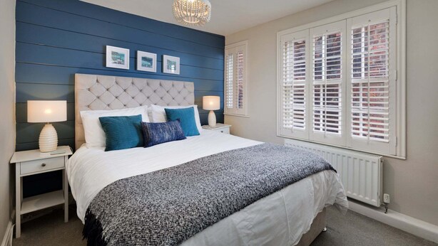 Ein Schlafzimmer mit einer gesteppten Kopfteil, einem großen Bett mit weißer und blauer Bettwäsche, zwei Nachttischlampen und einem Kronleuchter.