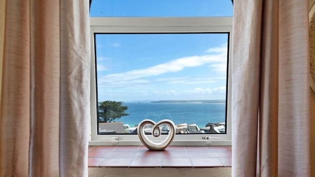 Une fenêtre ornée d’un motif en forme de cœur, une vue sur la mer et un sol carrelé.