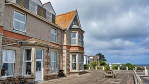 Une maison en pierre à deux étages, dotée d’une baie vitrée, d’un toit en tuiles et d’une terrasse dallée.