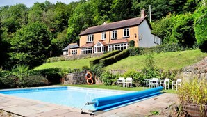 Une maison avec une piscine, entourée d’une végétation luxuriante et située au pied d’une colline.