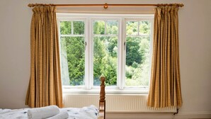 Une chambre avec un lit, une fenêtre avec des rideaux et une vue sur la verdure.