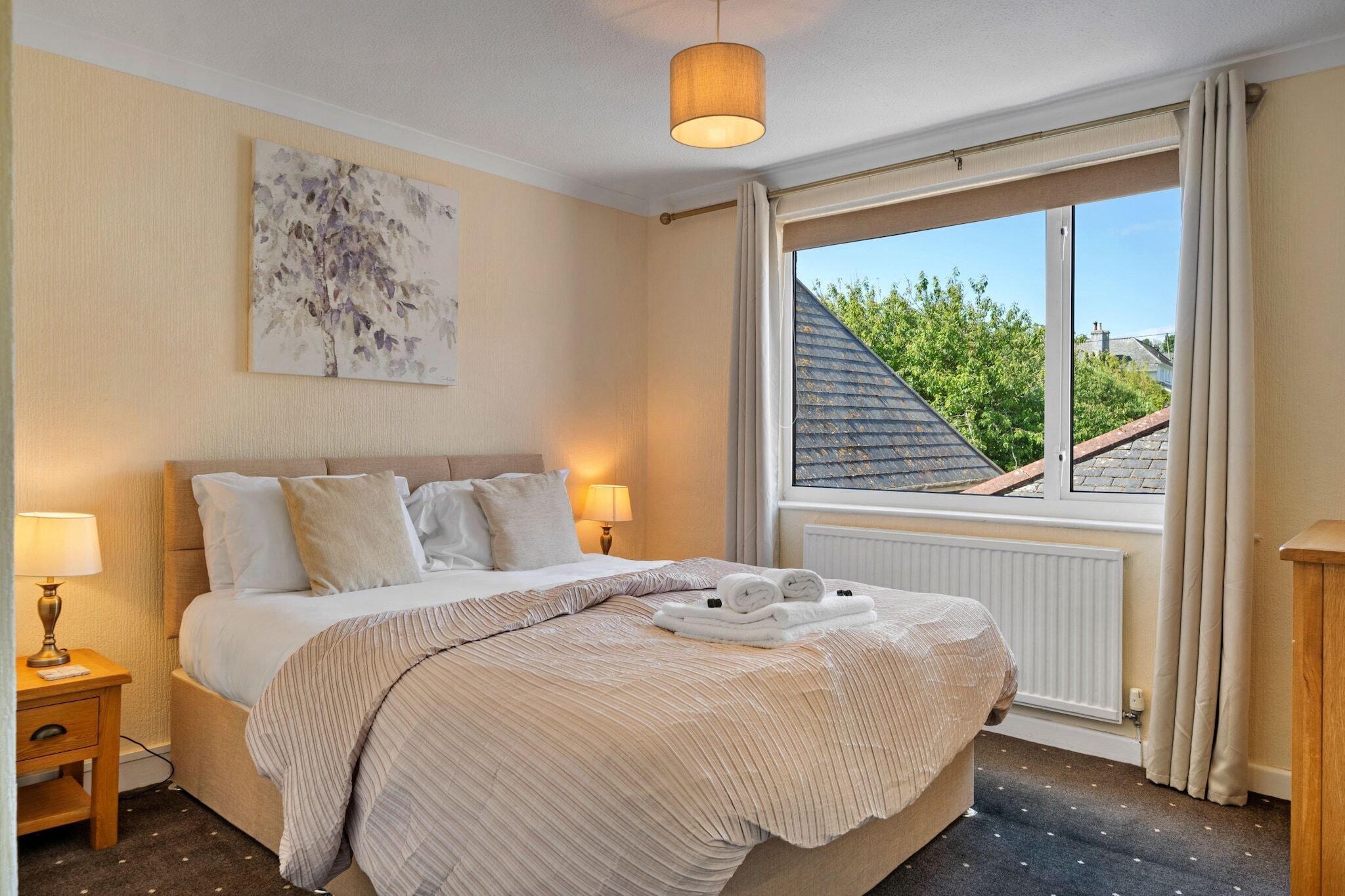 A neatly made bed with a striped bedspread and pillows, a bedside lamp, and a window with curtains.