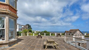 A terrace with picnic tables, a stone building, and a view of the sea.