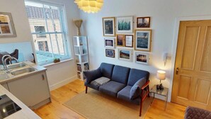 A modern kitchen with a built-in sink, a dining area with a grey sofa, and a wall decorated with framed pictures. - Apartment in Matlock near River Derwent (Matlock)